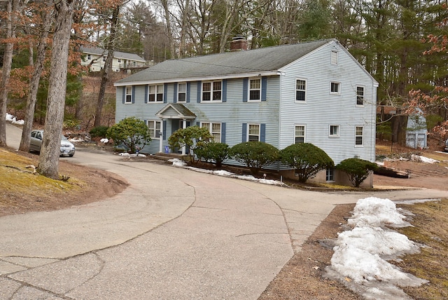 colonial home with roof with shingles, driveway, and a chimney