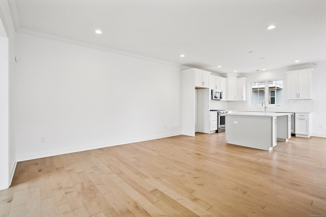 unfurnished living room featuring crown molding, light wood finished floors, a sink, and recessed lighting