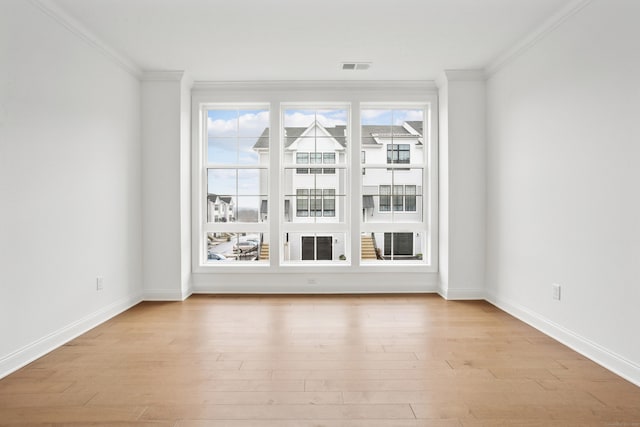 spare room with light wood-style floors, baseboards, visible vents, and crown molding