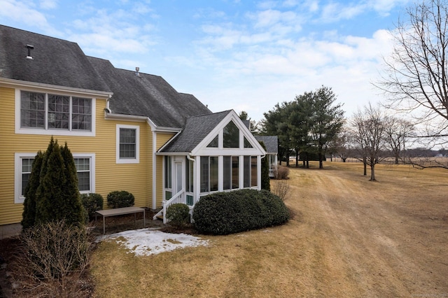 rear view of house with a sunroom, a shingled roof, and a yard