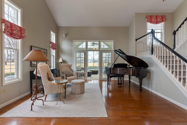 sitting room featuring a towering ceiling, stairway, baseboards, and wood finished floors