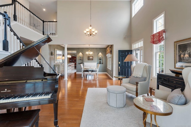 living area featuring ornate columns, an inviting chandelier, wood finished floors, baseboards, and stairs