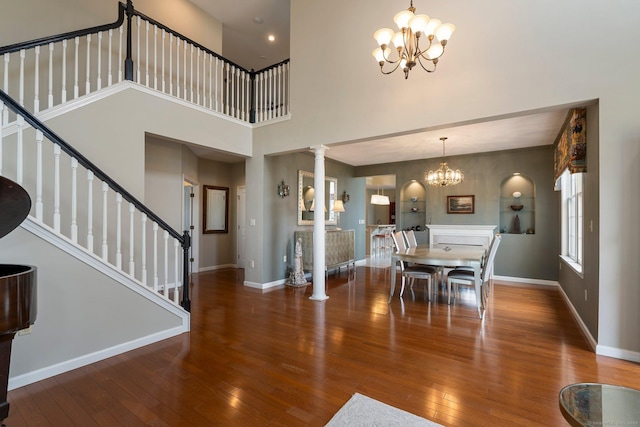 dining space with hardwood / wood-style flooring, a notable chandelier, baseboards, stairway, and ornate columns