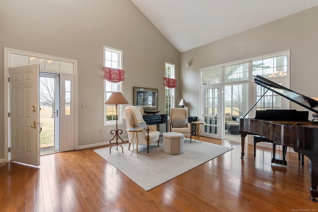 living area featuring high vaulted ceiling, baseboards, plenty of natural light, and hardwood / wood-style floors