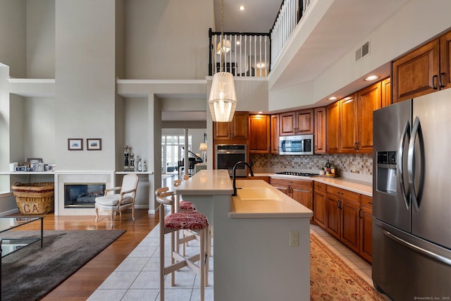 kitchen featuring a sink, visible vents, appliances with stainless steel finishes, brown cabinets, and a glass covered fireplace