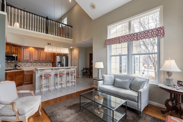 living area with light wood-style floors, visible vents, a high ceiling, and baseboards