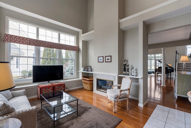 living area featuring decorative columns, a high ceiling, wood finished floors, and a glass covered fireplace