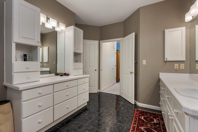 bathroom featuring two vanities, a sink, and baseboards