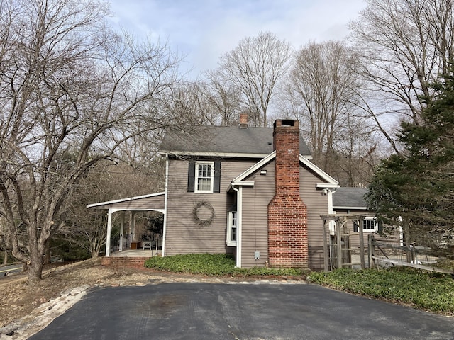 view of front of home featuring a carport, a chimney, and a shingled roof