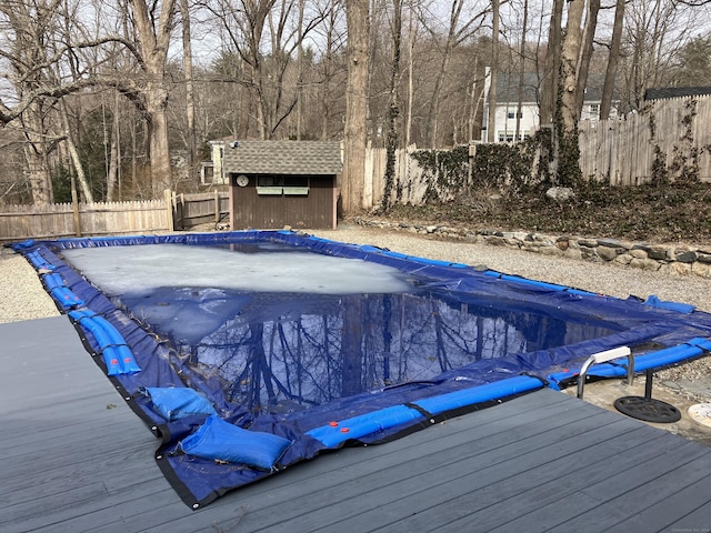 view of swimming pool with a deck, an outbuilding, a fenced backyard, and a shed