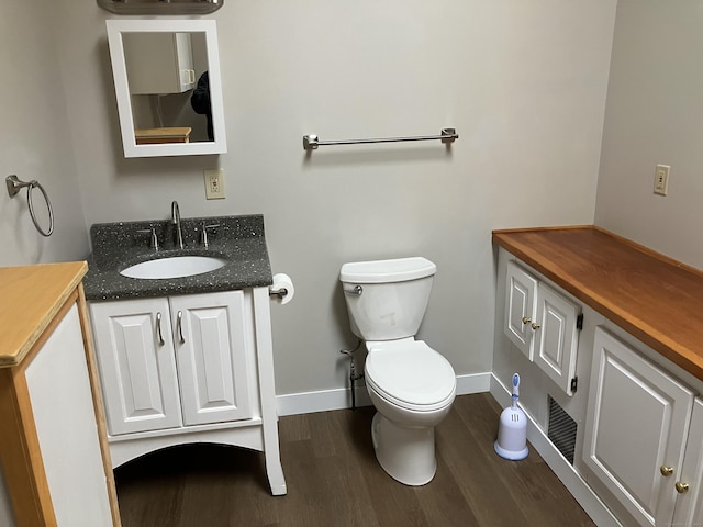 half bathroom with vanity, toilet, wood finished floors, and baseboards