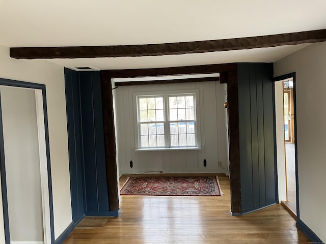 spare room featuring beam ceiling, wood finished floors, and baseboards