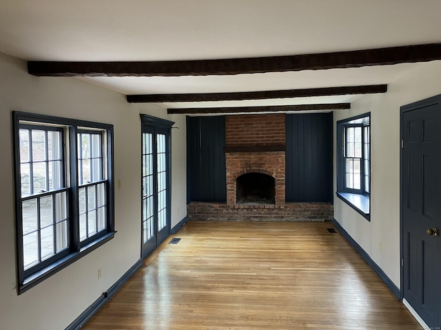 unfurnished living room featuring beamed ceiling, visible vents, light wood-style floors, a fireplace, and baseboards