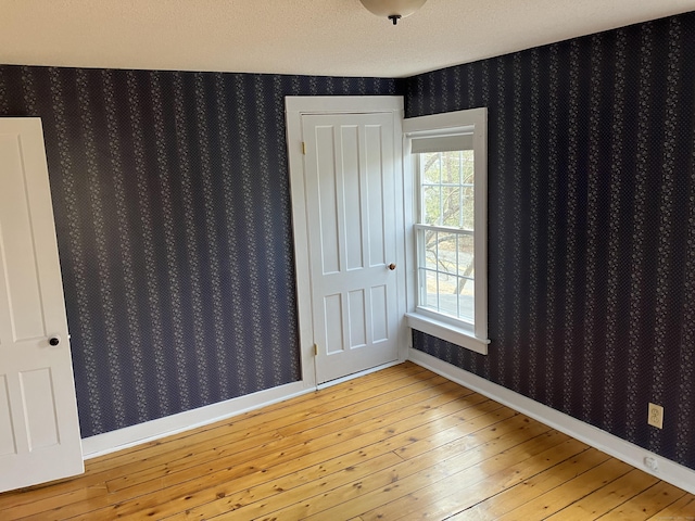 spare room featuring baseboards, light wood-style floors, and wallpapered walls