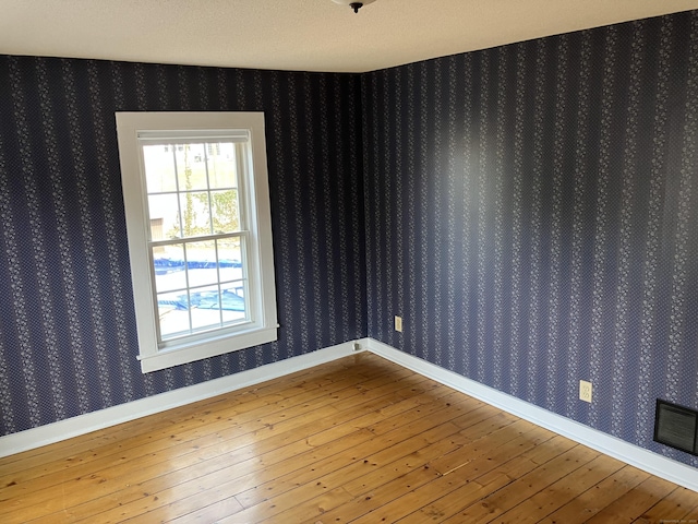 unfurnished room with wallpapered walls, hardwood / wood-style flooring, and baseboards