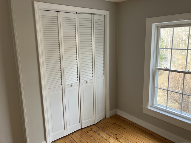 unfurnished bedroom featuring a closet, multiple windows, light wood-style flooring, and baseboards