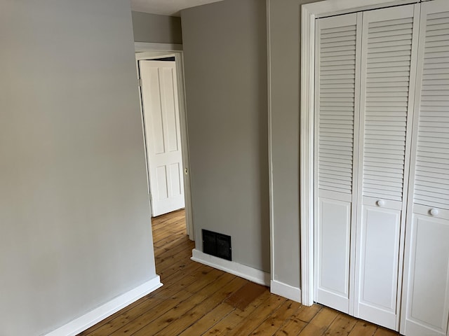 unfurnished bedroom with a closet, visible vents, baseboards, and wood-type flooring