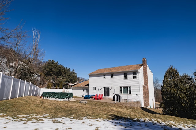 snow covered house with a fenced in pool, a patio, a chimney, fence, and cooling unit