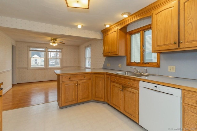 kitchen with wallpapered walls, a peninsula, white dishwasher, a sink, and light countertops