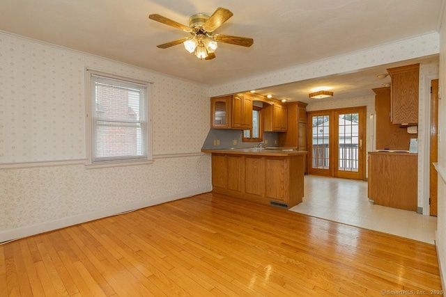 kitchen featuring brown cabinetry, a peninsula, wallpapered walls, and light wood-style floors