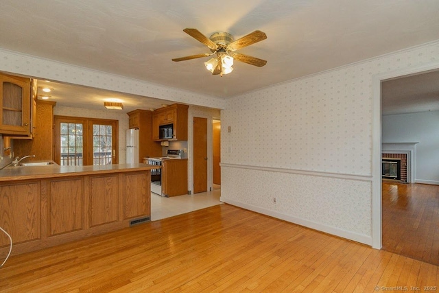 kitchen featuring brown cabinets, wallpapered walls, range with electric stovetop, freestanding refrigerator, and light wood finished floors