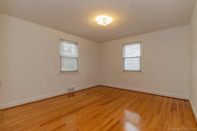 spare room featuring light wood finished floors, visible vents, and baseboards