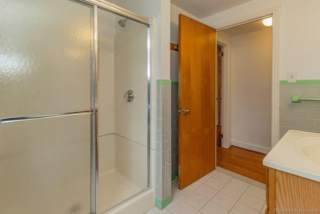 full bathroom featuring a stall shower, tile walls, wainscoting, tile patterned flooring, and vanity