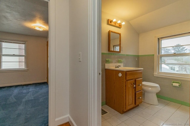 bathroom featuring toilet, tile walls, tile patterned flooring, lofted ceiling, and vanity