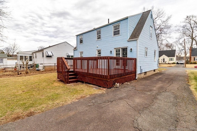 rear view of property with a yard, roof with shingles, a wooden deck, and aphalt driveway