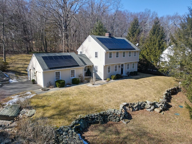 rear view of property with roof mounted solar panels, a lawn, a chimney, and an attached garage