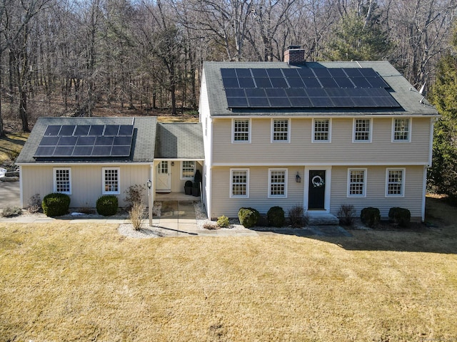 colonial inspired home with a front lawn, roof mounted solar panels, and a chimney