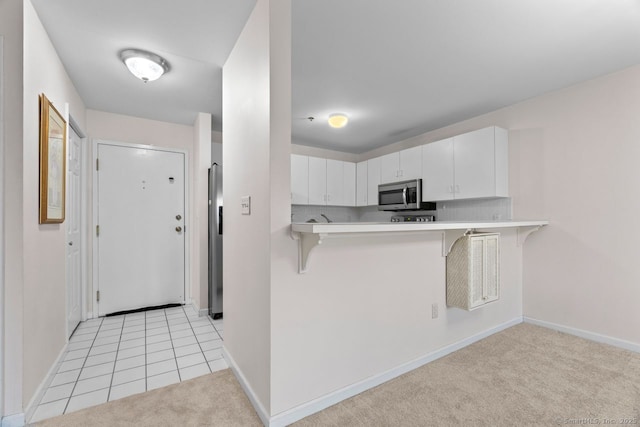 kitchen featuring stainless steel appliances, light countertops, white cabinets, light carpet, and a kitchen breakfast bar