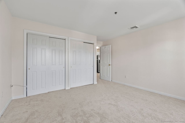 unfurnished bedroom featuring visible vents, multiple closets, light colored carpet, and baseboards