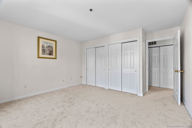 unfurnished bedroom featuring light colored carpet, visible vents, two closets, and baseboards