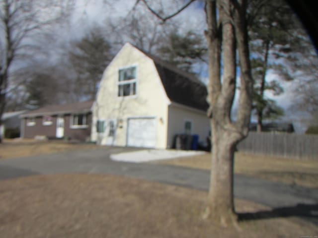 exterior space with a garage, driveway, a gambrel roof, and fence