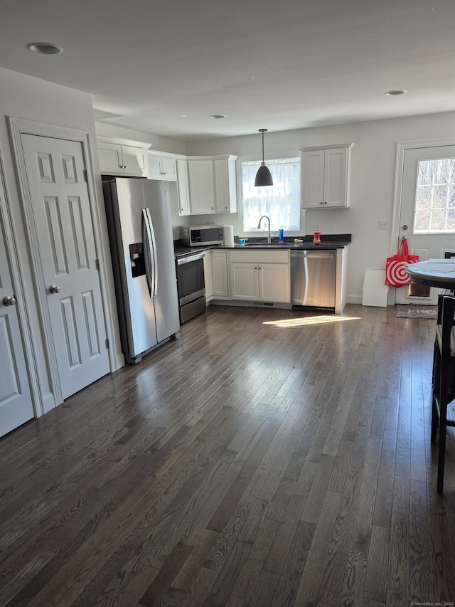 kitchen with dark wood-style floors, a sink, stainless steel appliances, pendant lighting, and dark countertops