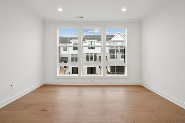 empty room featuring light wood-style floors, visible vents, crown molding, and baseboards