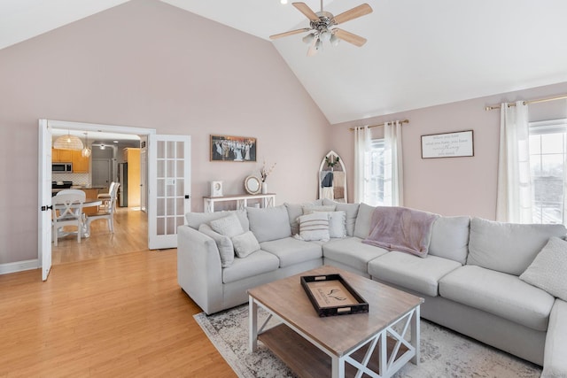 living area with light wood finished floors, high vaulted ceiling, french doors, and a ceiling fan