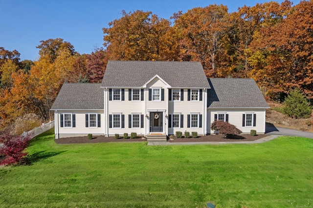 colonial inspired home with a shingled roof, fence, and a front yard