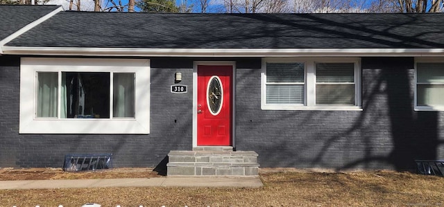 entrance to property featuring roof with shingles and brick siding