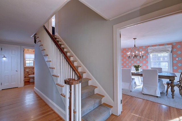 stairway featuring an inviting chandelier, wallpapered walls, baseboards, and hardwood / wood-style flooring