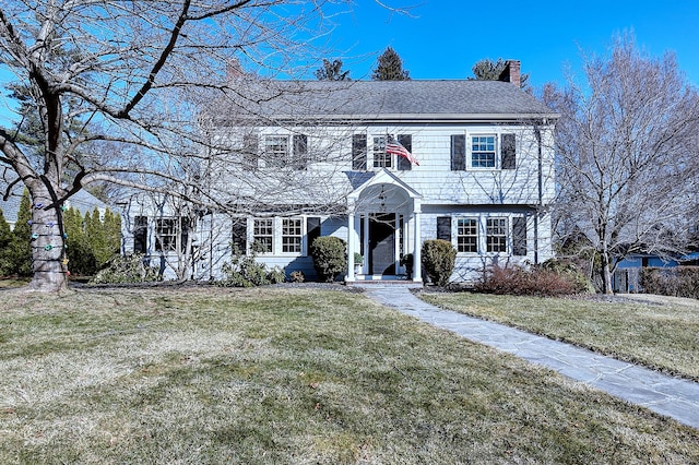 colonial-style house featuring a chimney and a front lawn