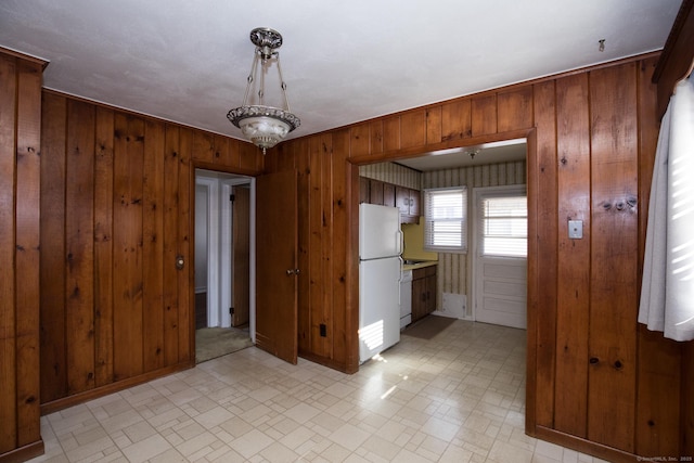 interior space with white appliances, light floors, baseboards, and wood walls