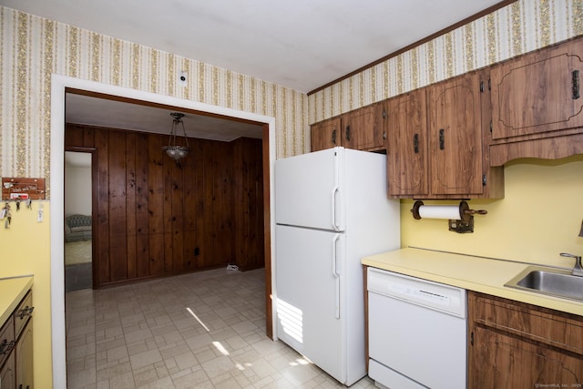 kitchen featuring brown cabinets, a sink, wallpapered walls, white appliances, and light countertops