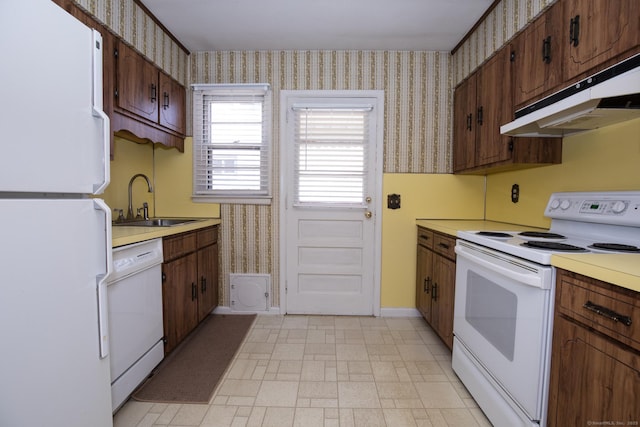 kitchen with white appliances, wallpapered walls, a sink, light countertops, and under cabinet range hood