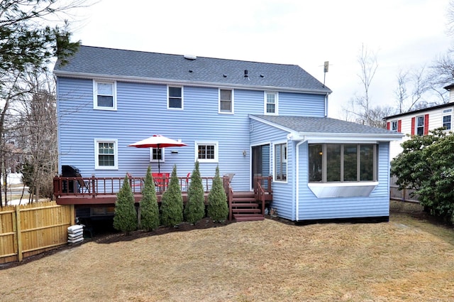 rear view of property featuring roof with shingles, fence, a deck, and a yard