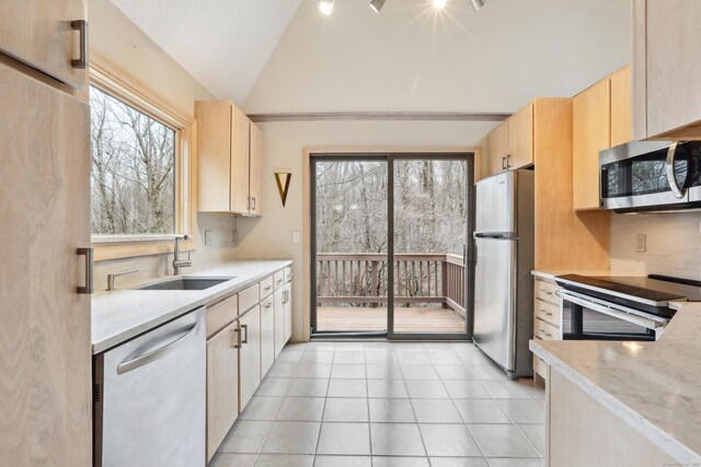 kitchen featuring light brown cabinets, appliances with stainless steel finishes, vaulted ceiling, and backsplash