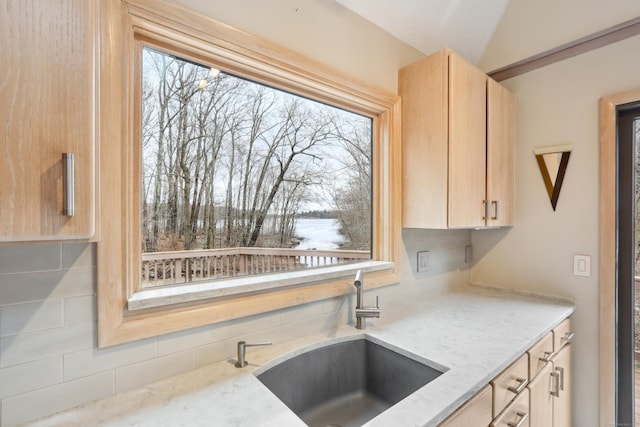 kitchen featuring a sink, light brown cabinets, lofted ceiling, and light stone countertops