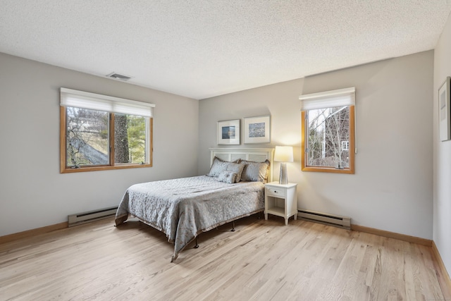 bedroom featuring a baseboard heating unit, visible vents, light wood-style flooring, and a textured ceiling