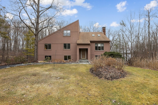 rear view of property featuring a shingled roof, a chimney, and a lawn